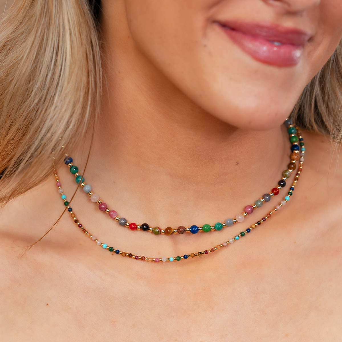 Model wearing a healing necklace stack. The necklaces include a 2mm multicolor stone and gold bead healing necklace and a 4mm multicolor stone and gold bead healing necklace