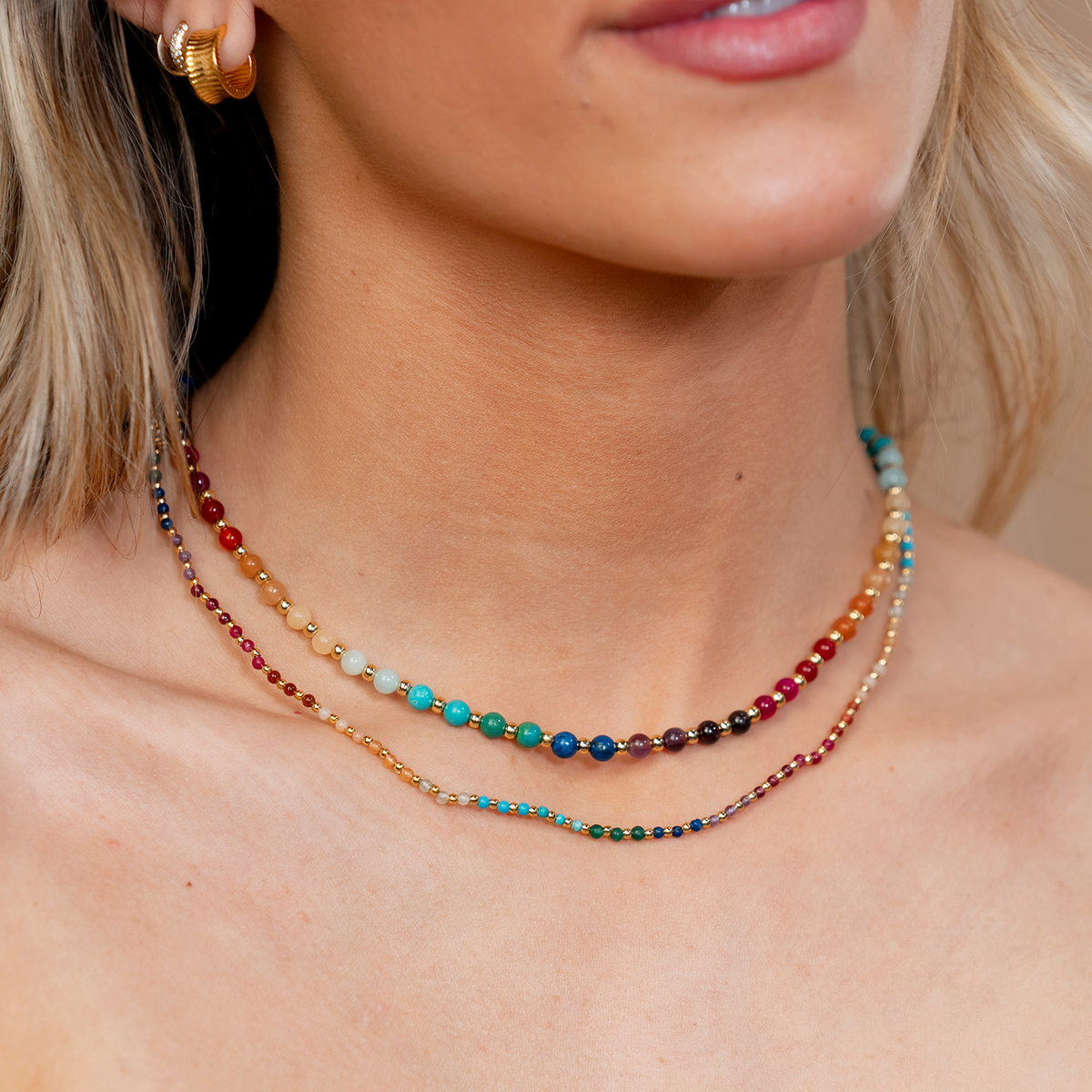 Model wearing a necklace stack. The necklaces include a 2mm multicolor stone and gold bead healing necklace and a 4mm multicolor stone and gold bead healing necklace