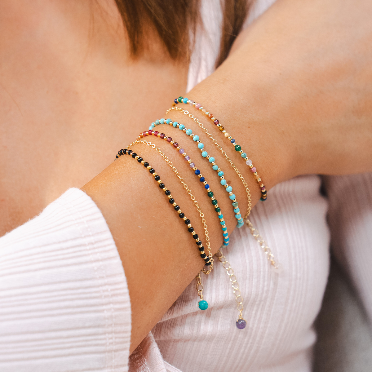 Dainty bracelet with assorted multi-color stones and gold beads pictured with a stack of turquoise, onyx and multi-colored bracelets