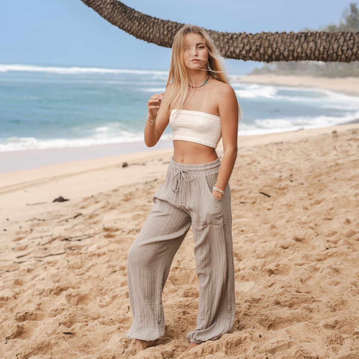 Model standing on the beach wearing stone colored harem pants with a drawstring waistband