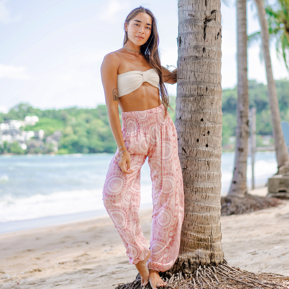 Girl standing next to a tree on the beach wearing light pink mandala print harem pants