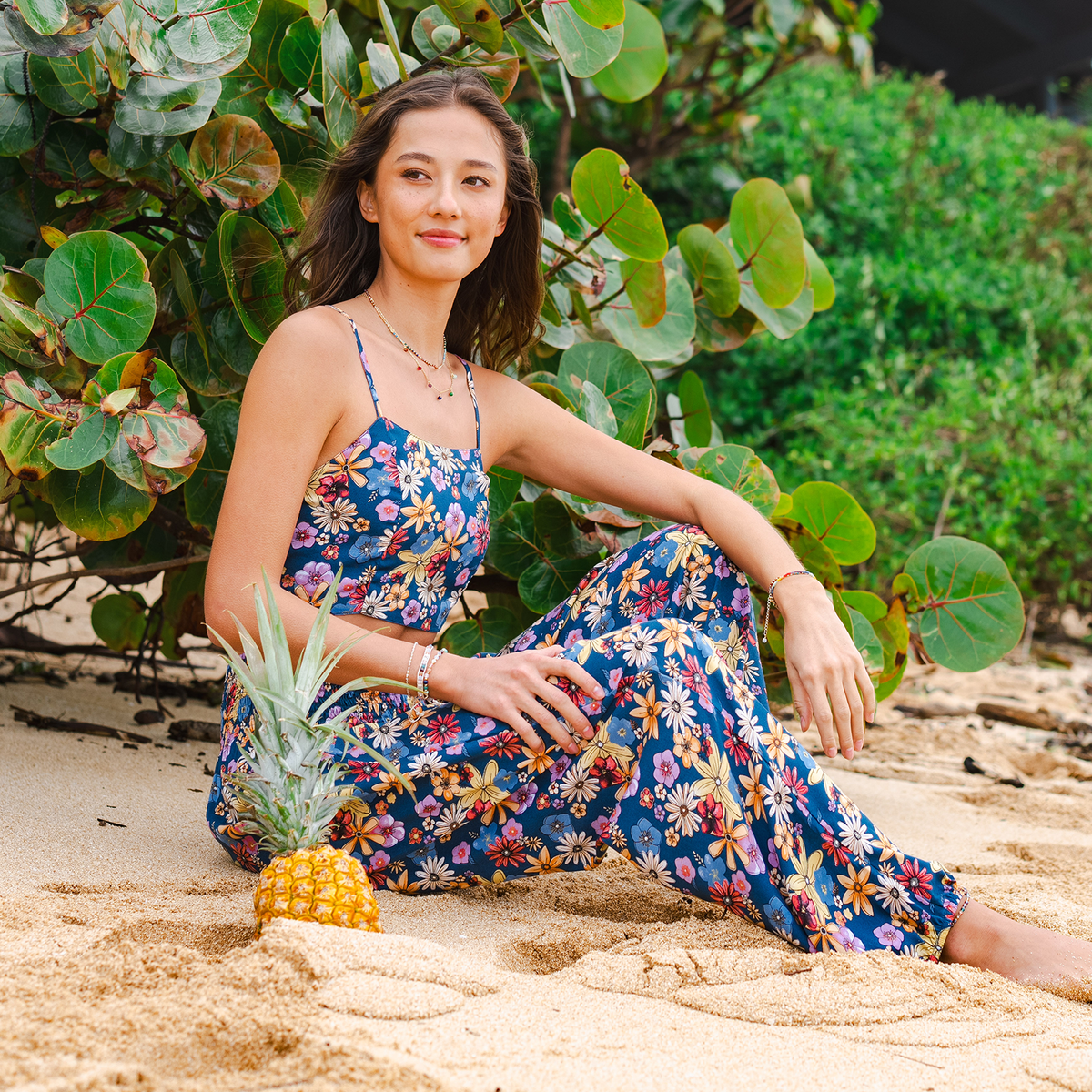 Model sitting on the beach wearing blue, pink, orange and yellow floral print harem pants