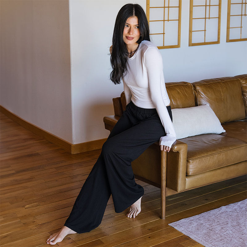 White Modal Halo Long Sleeve Top and Black Modal Sway Wide Leg Pants, leaning on sofa arm