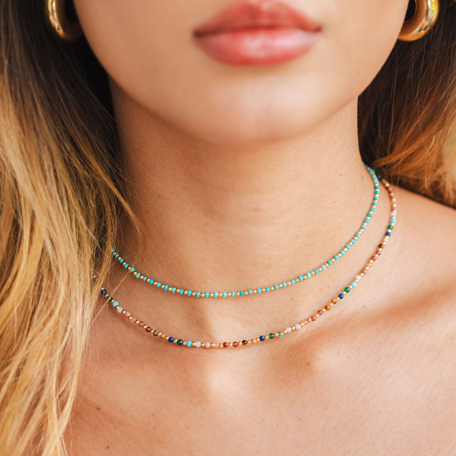Model wearing a stack of two healing necklaces. The necklaces include a 2mm multicolor stone and gold bead healing necklace and a 2mm turquoise stone and gold bead healing necklace