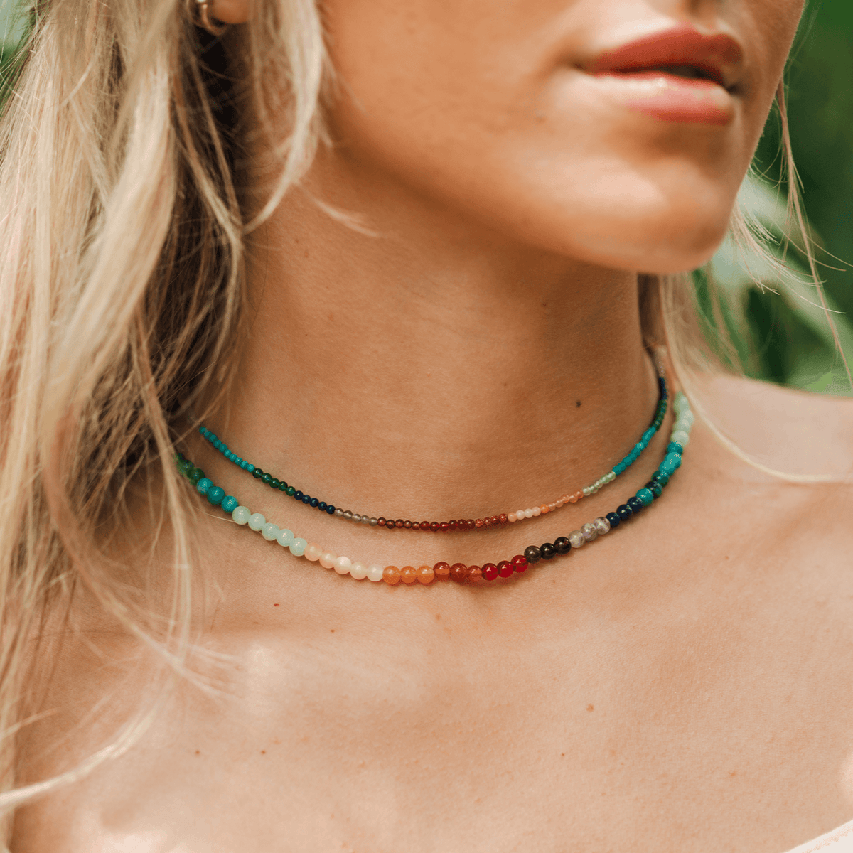 Girl wearing a necklace stack with 2mm and 4mm rainbow beaded necklaces
