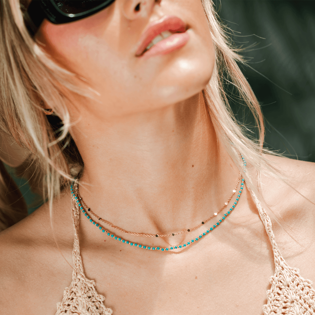 Model wearing necklace stack with a turquoise bead necklace and a simple gold chain necklace