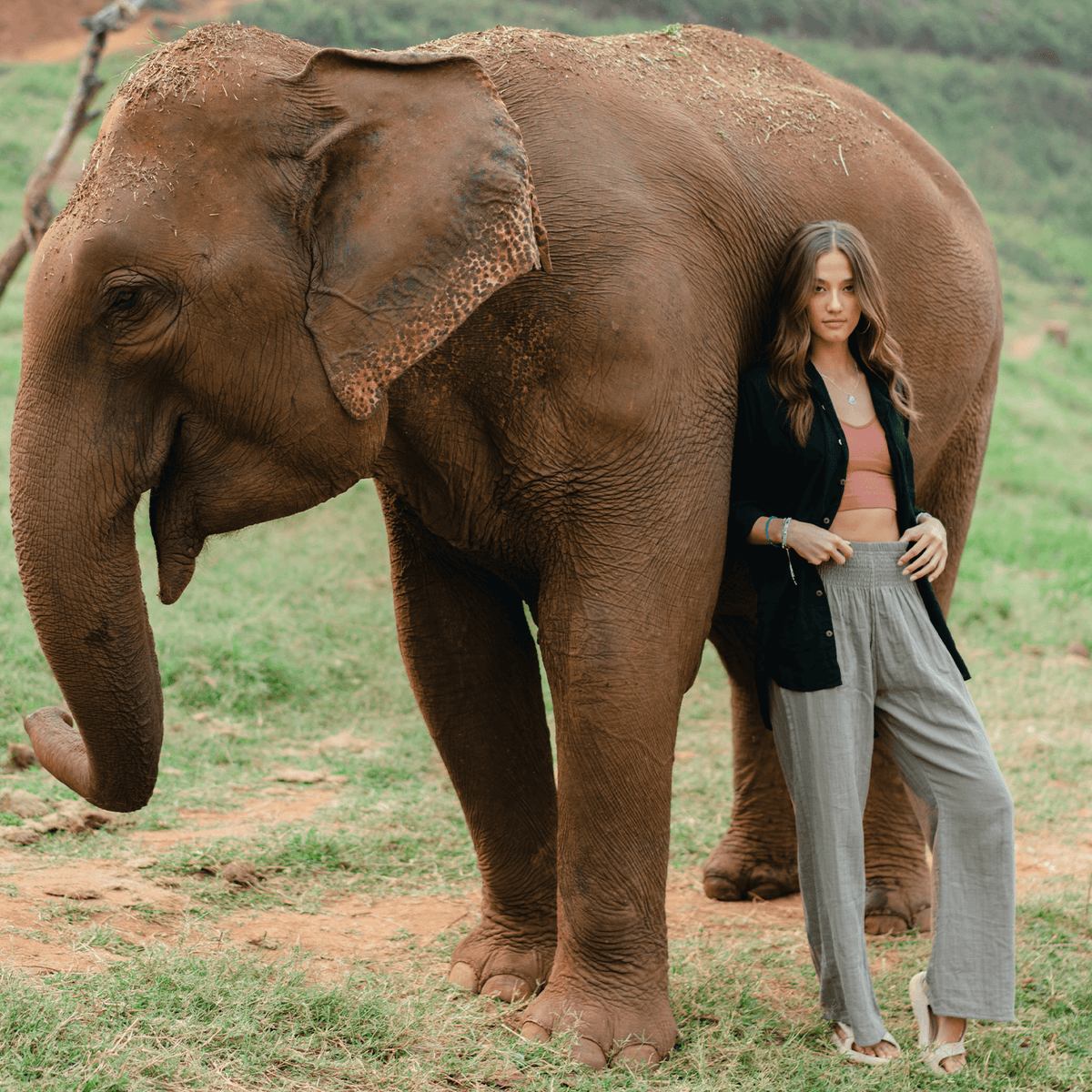 Girl wearing gray wide leg cotton pants leaning against an elephant