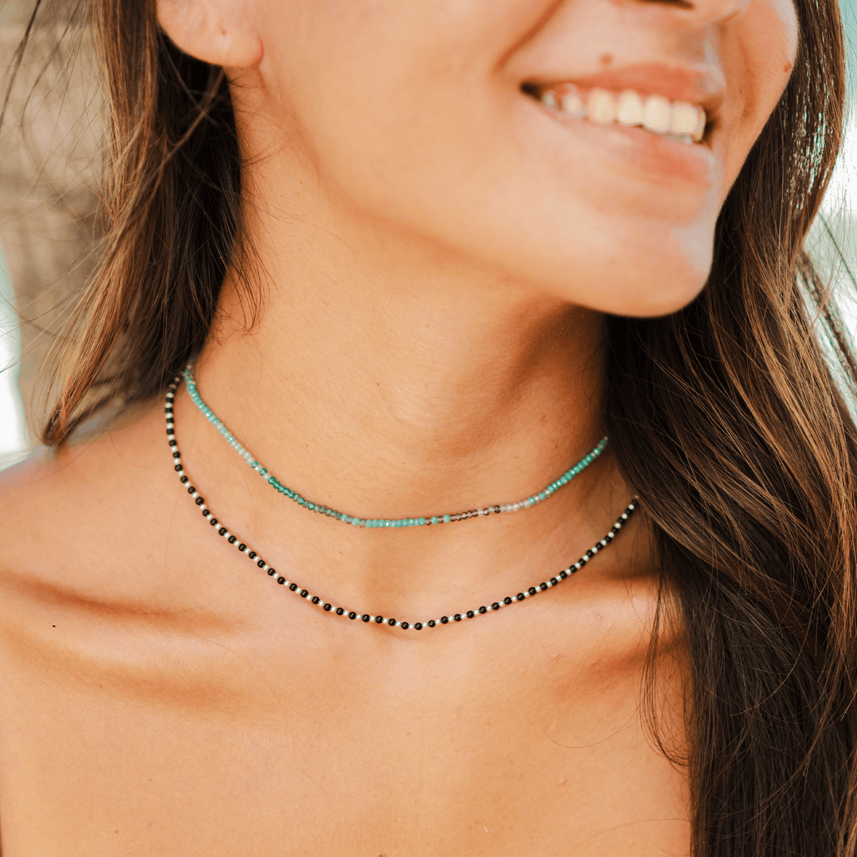 Model wearing a stack of two necklaces. One is a teal and blue stone goddess necklace and the other is a onyx healing stone necklace