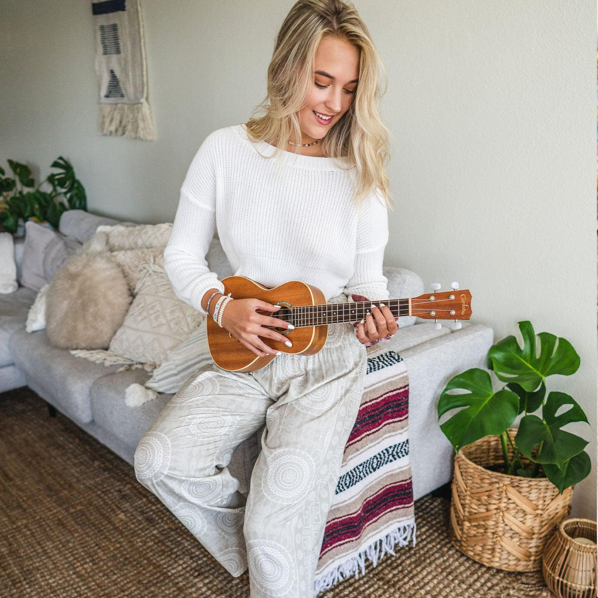 Model playing the ukulele while wearing cream and white mandala print harem pants