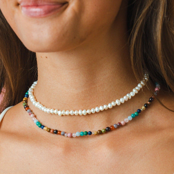 Model wearing a stack of two healing necklaces. The necklaces include a pearl healing necklace and a 4mm multicolor stone healing necklace