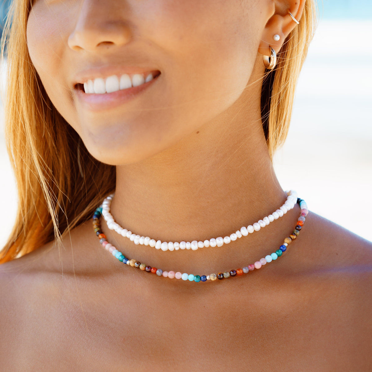 Model wearing a stack of two healing necklaces. The necklaces include a pearl healing necklace and a 4mm multicolor stone healing necklace