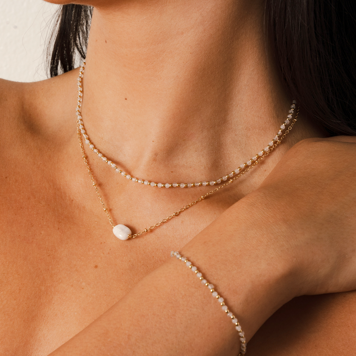 Model wearing a necklace stack. The stack consists of a 2mm moonstone and gold bead healing necklace and a moonstone healing necklace with a gold chain. She is also wearing a 2mm moonstone and gold bead healing bracelet