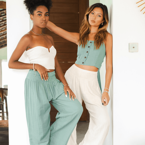 Two models standing next to each other. One is wearing cream wide leg cotton pants and the other is wearing sage wide leg cotton pants